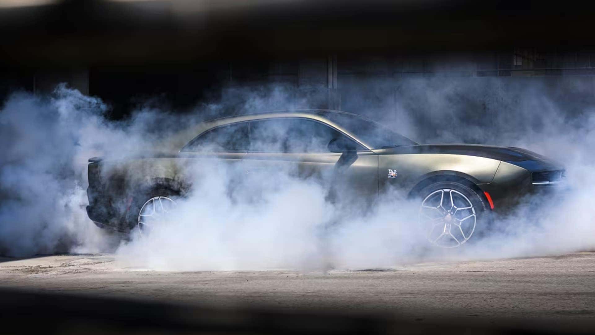 Dark two-door Dodge Charger shown in side profile surrounded by thick tire smoke on a paved surface.