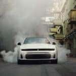 White Dodge Charger facing forward in an industrial alley with smoke surrounding the rear and sides.