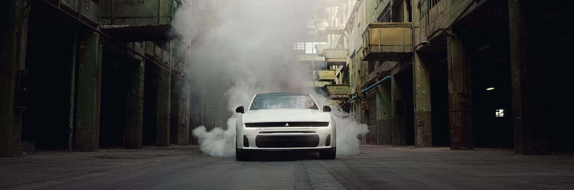 White Dodge Charger facing forward in an industrial alley with smoke surrounding the rear and sides.