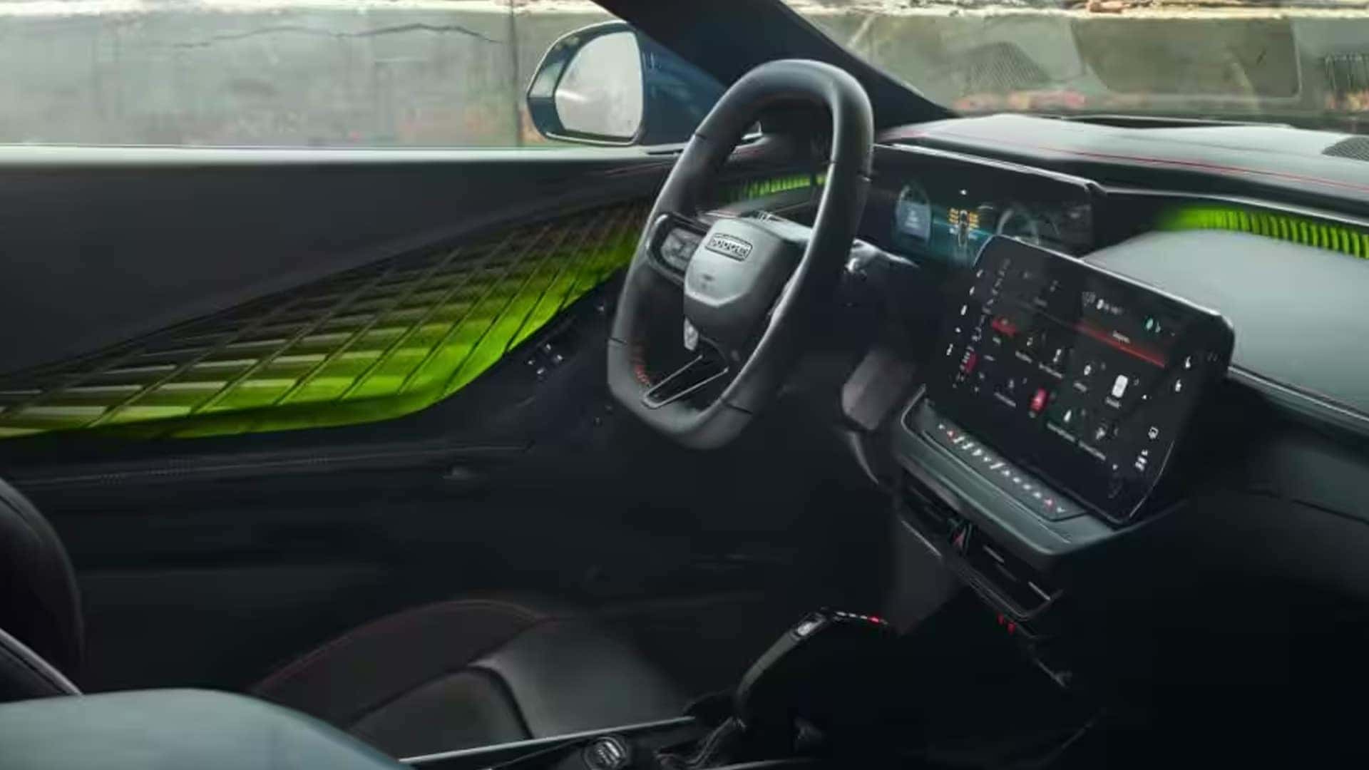 Front cabin with black seats, steering wheel, center touchscreen, and bright green lighting across the door and dash.