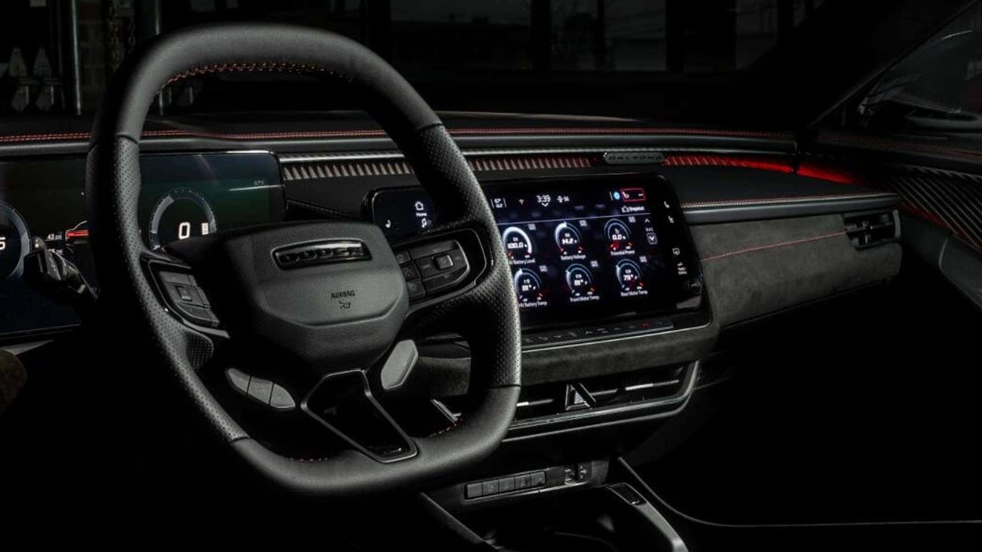 Black steering wheel in front of a digital gauge cluster and center touchscreen with red dashboard accent lighting.
