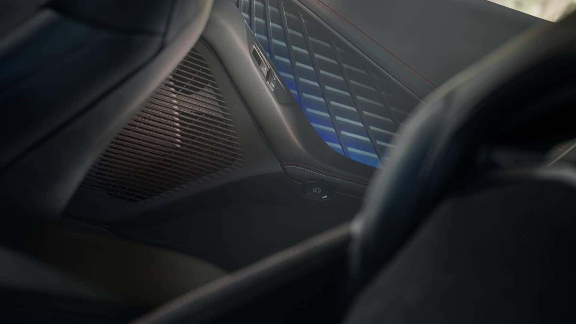 Close-up of a large speaker grille and blue accent lighting on the interior side panel behind the front seats.