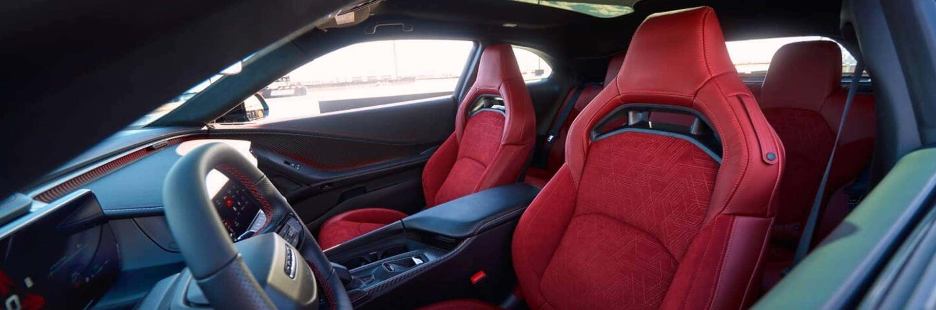 Red front sport seats, black dashboard, steering wheel, center console, and glass roof inside a 2026 Dodge Charger.