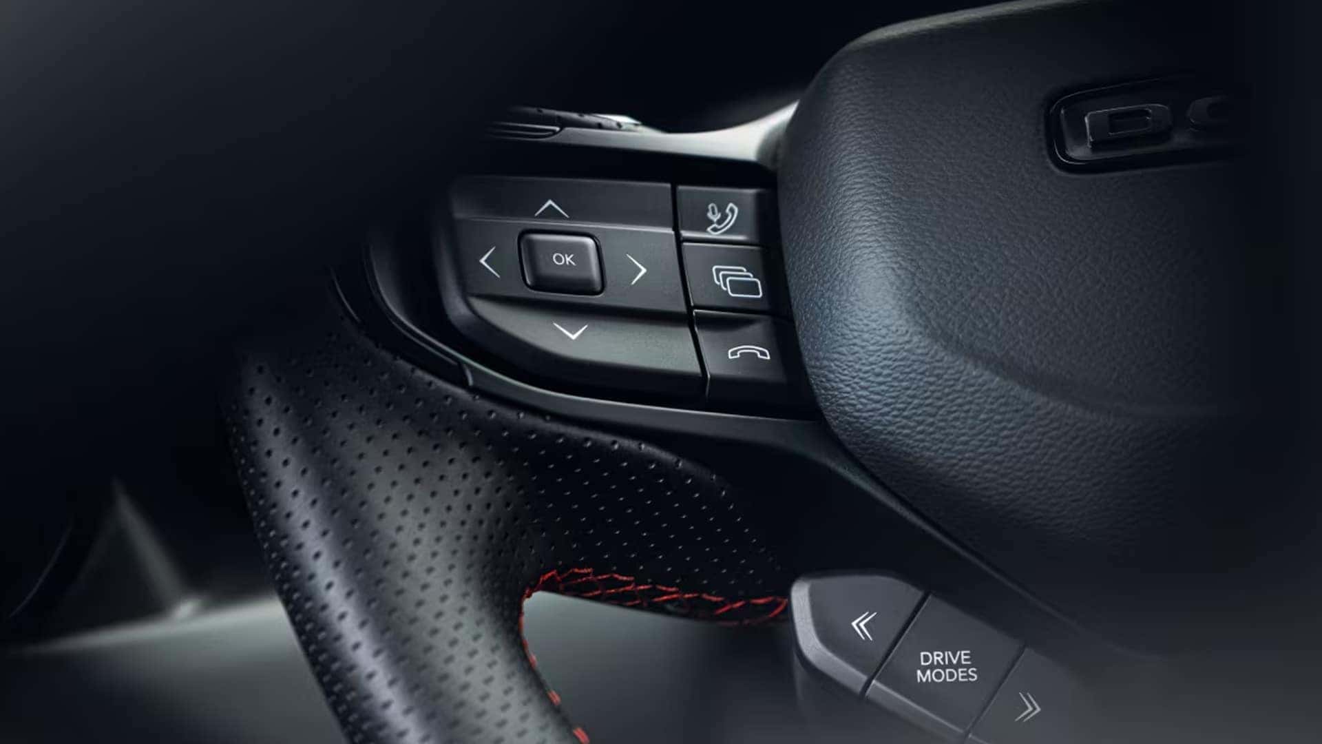 Close-up of a black steering wheel with phone, menu, arrow, and Drive Modes control buttons.