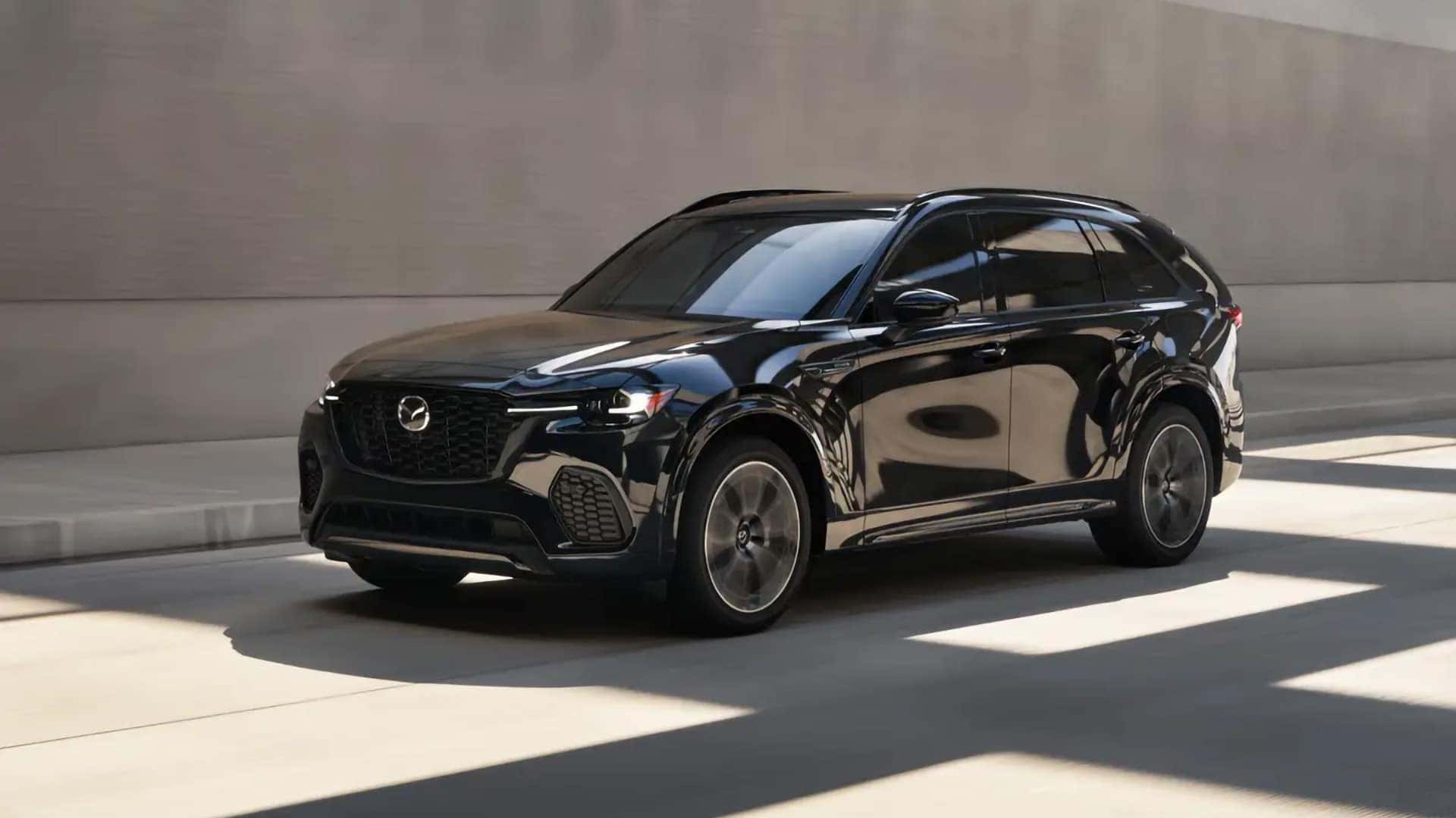 Black 2026 Mazda CX-70 PHEV driving with its LED headlights illuminated