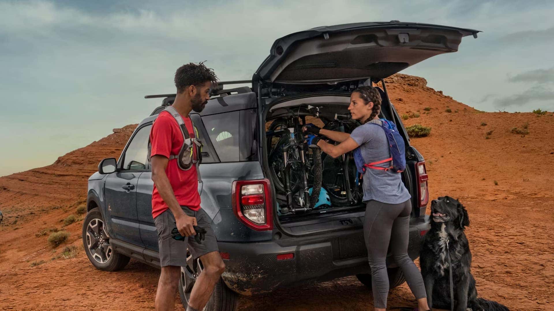 Cyclists loading bicycles into the rear cargo area of a 2026 Ford Bronco Sport beside a desert trail