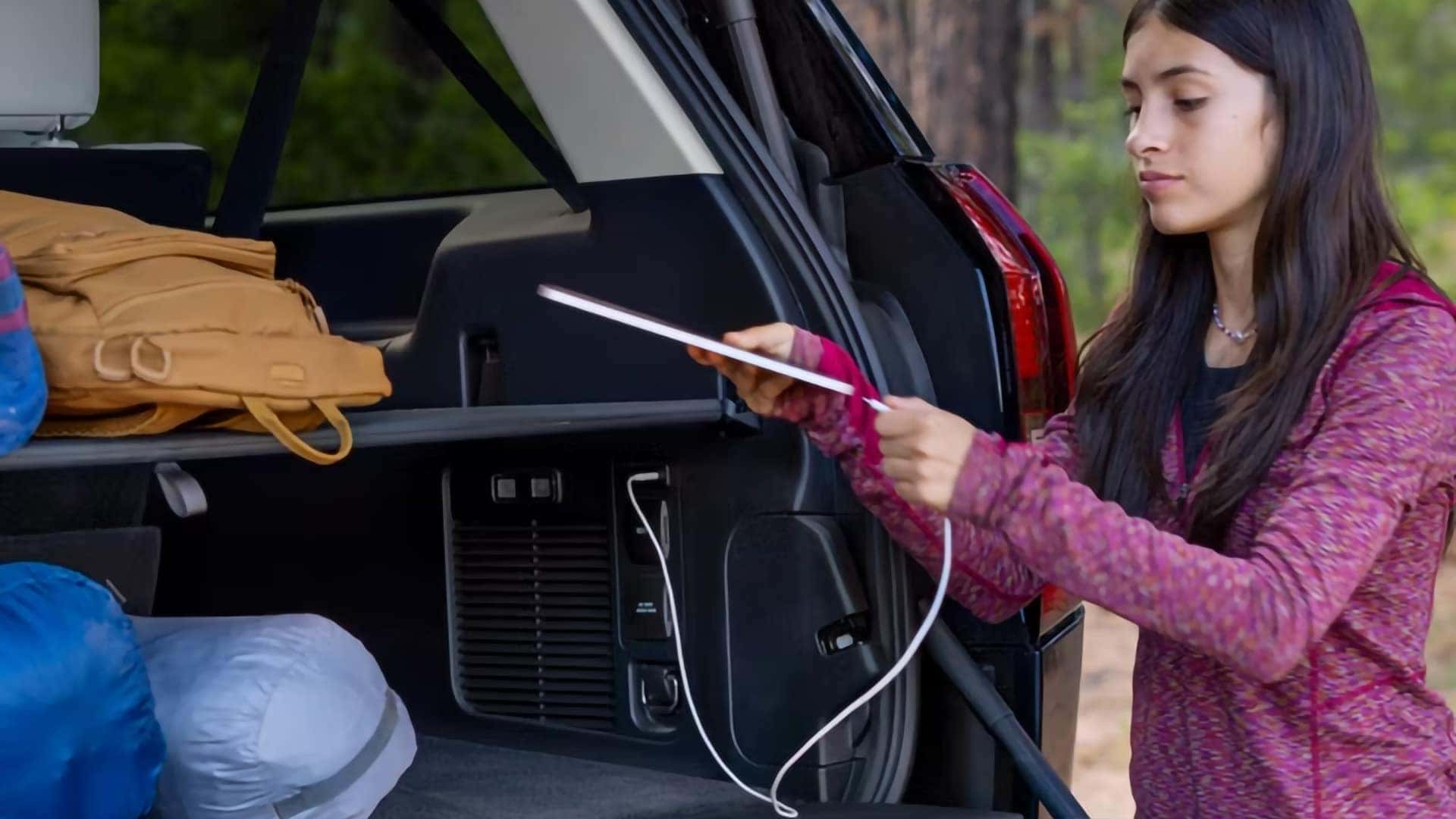 Passenger connecting a device to a charging outlet in the cargo area of a 2026 Ford Expedition