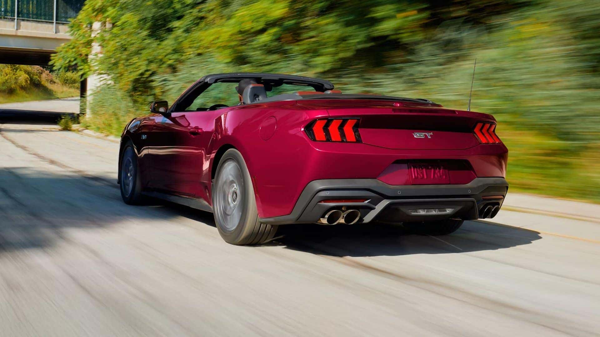 Red 2026 Ford Mustang GT Convertible accelerating on a tree-lined road