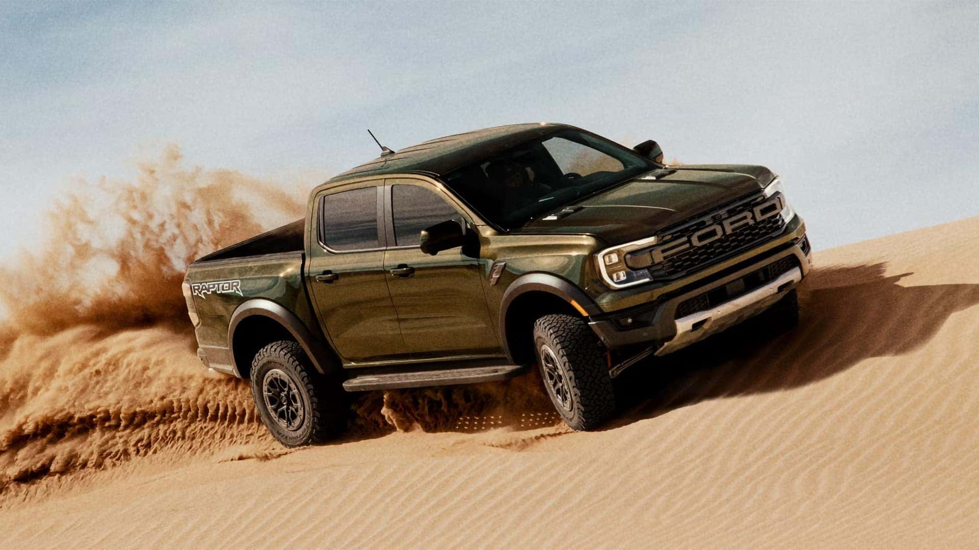 2026 Ford Ranger Raptor driving through sand with off-road tires, flared fenders, and FORD grille