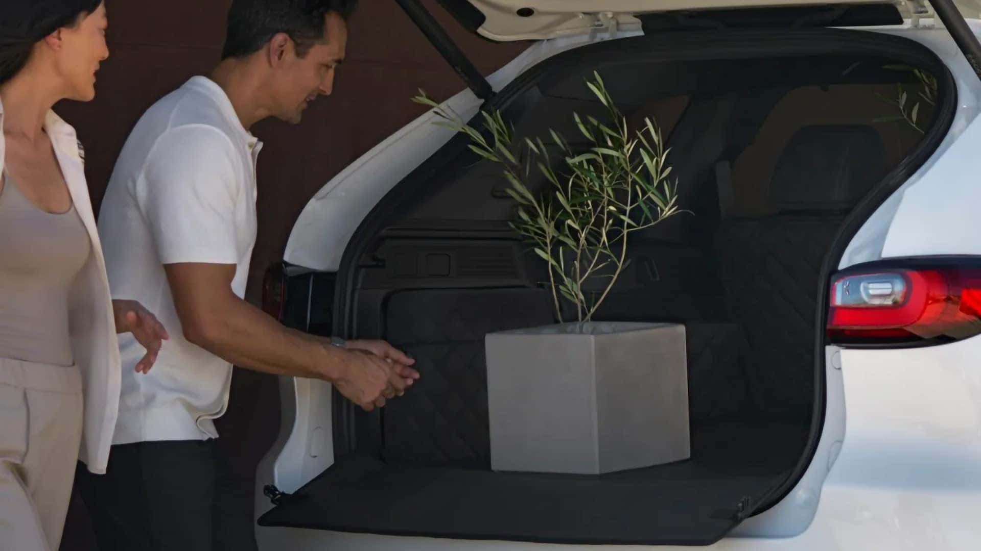 Couple loading a potted plant into the cargo area of a white 2026 Mazda CX-70 PHEV