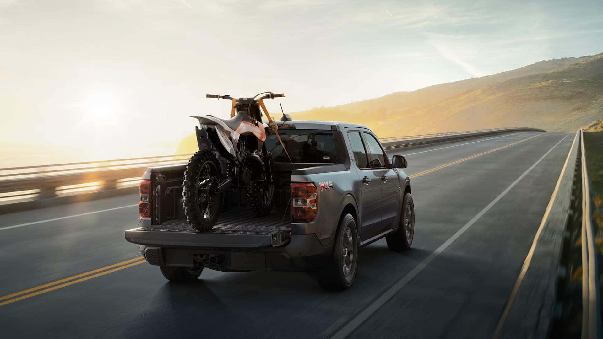Gray Ford Maverick carrying a dirt bike in its open bed with the tailgate lowered