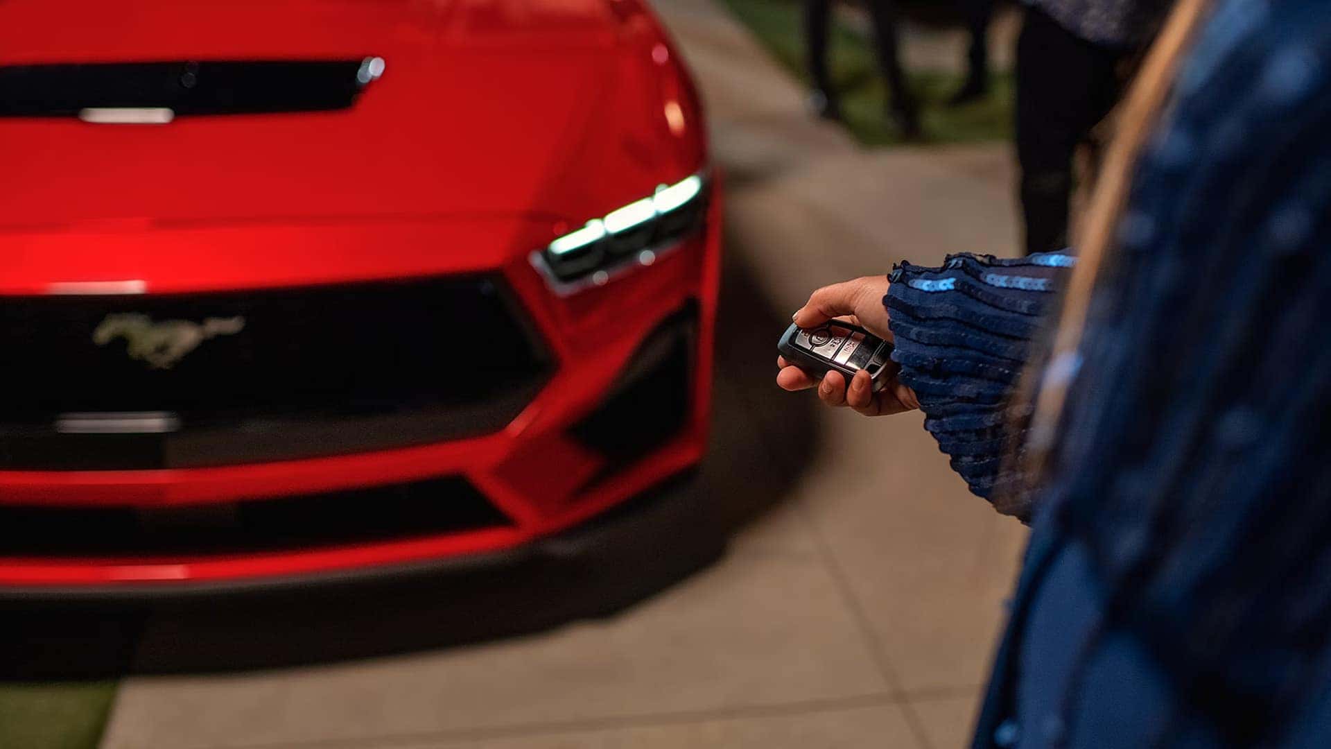 Driver using a key fob near a red 2026 Ford Mustang to access Remote Rev and vehicle functions