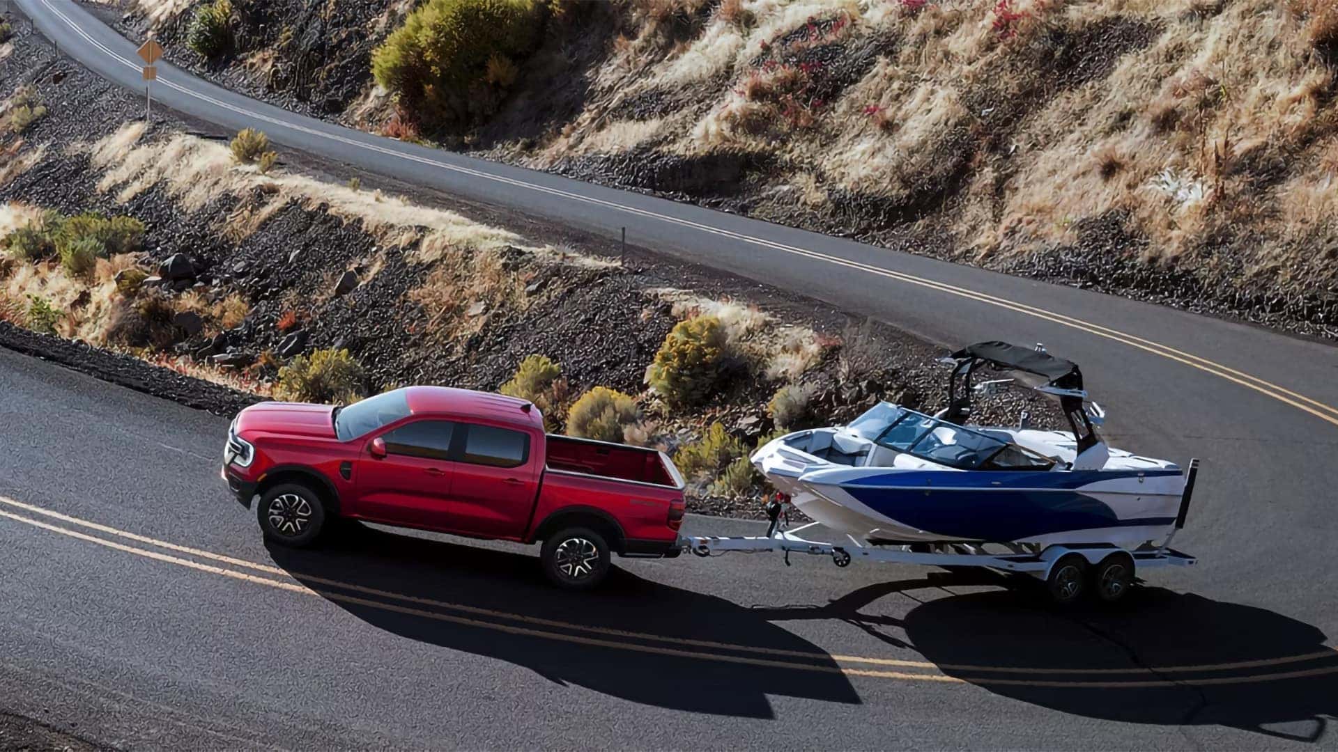 Red 2026 Ford Ranger towing a boat on a trailer along a mountain road