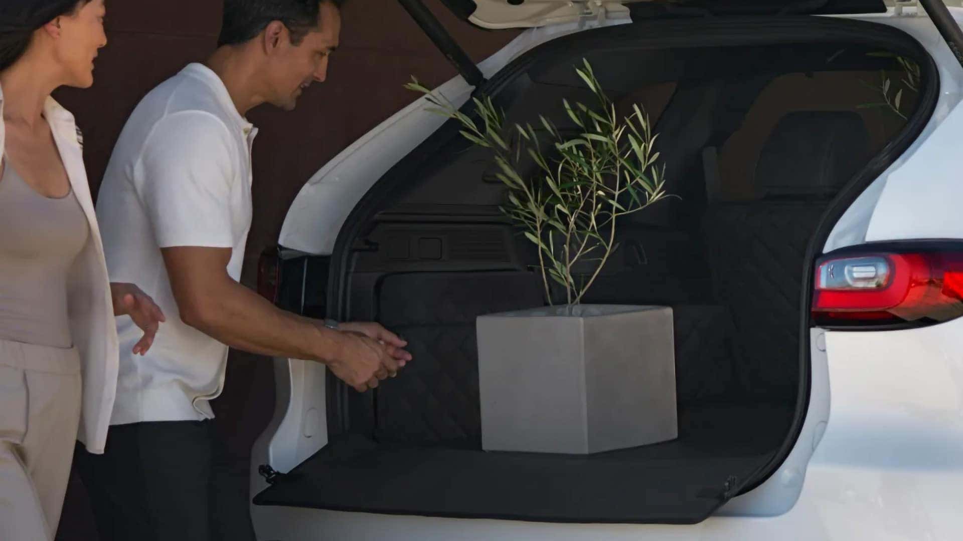 Couple loading a potted plant into the open cargo area of a white 2026 Mazda CX-70 PHEV