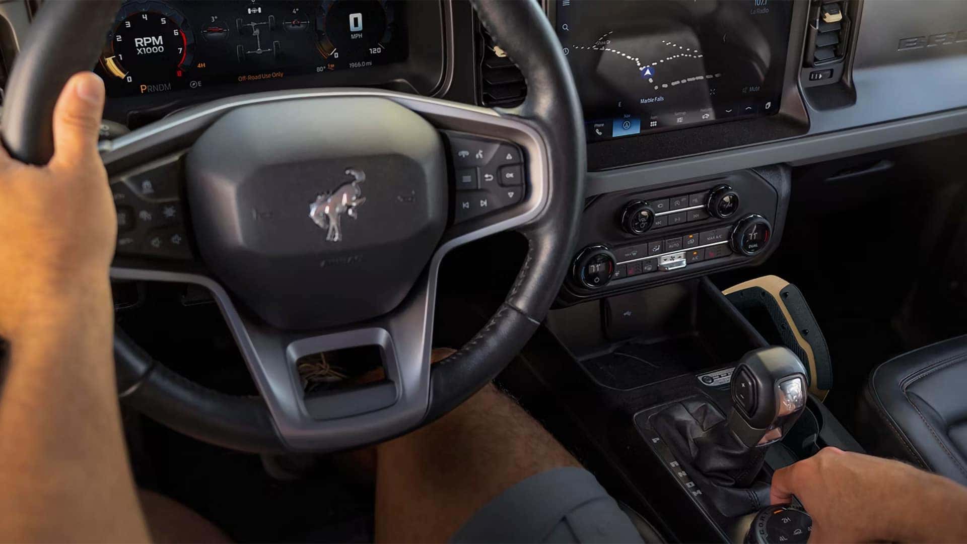 Driver operating a 2026 Ford Bronco with the digital instrument cluster and navigation touchscreen visible
