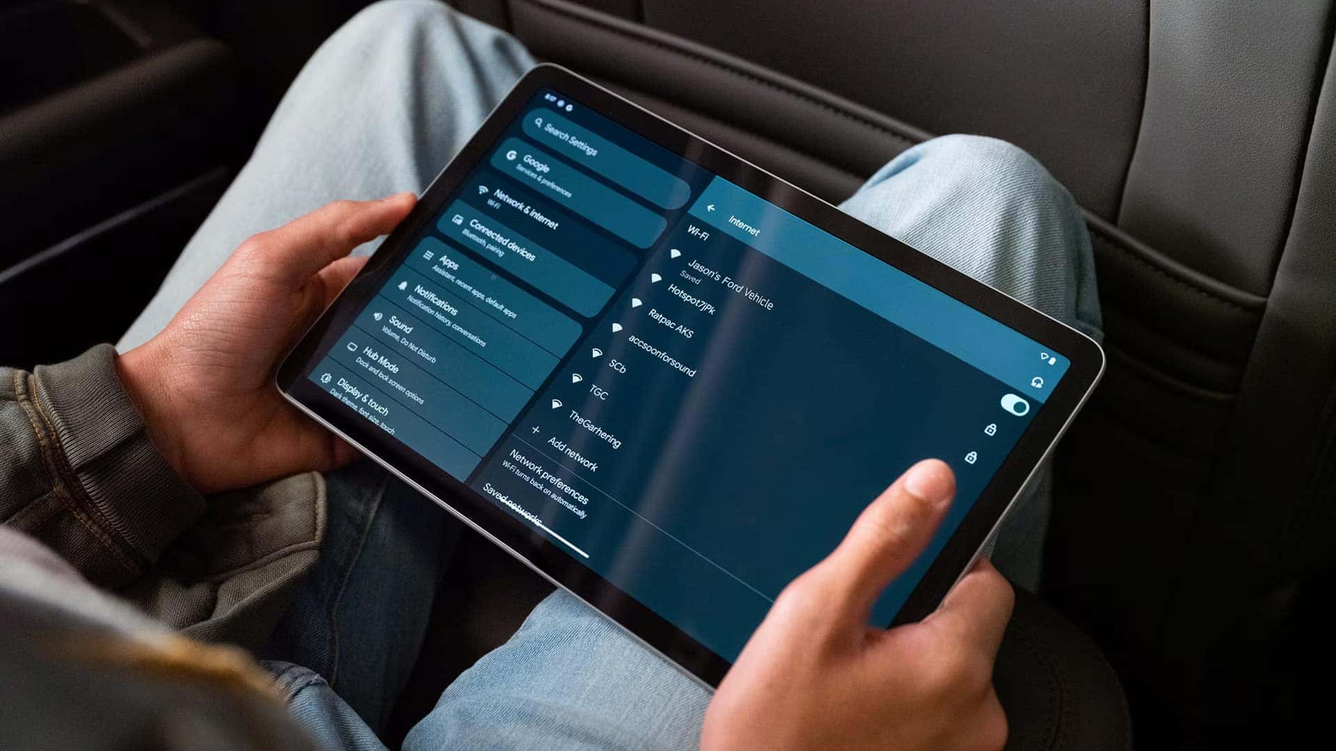 Passenger holding a tablet with Wi-Fi settings showing a saved Ford vehicle hotspot network