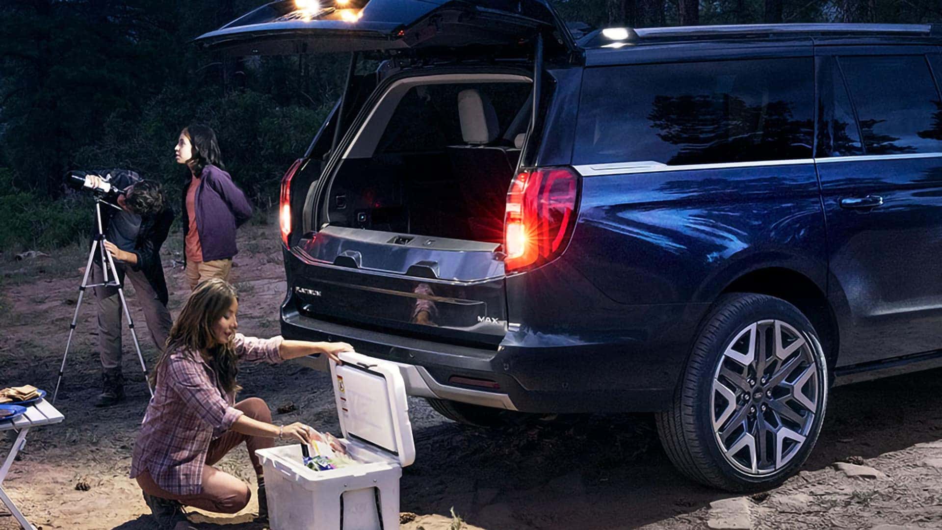 Blue 2026 Ford Expedition MAX at a campsite with the Split Gate open and exterior lights illuminated