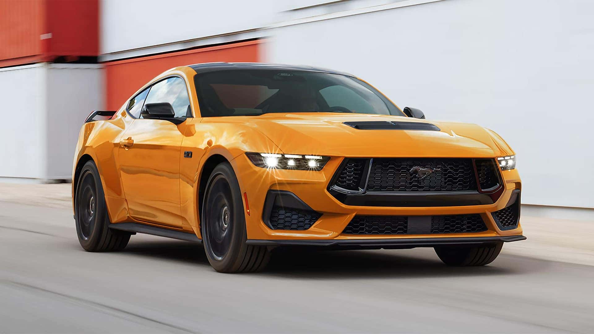 Orange 2026 Ford Mustang fastback showing front styling, black wheels, grille, and hood details