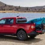 Red Ford Maverick XLT parked by a lake with kayaks secured in its cargo bed