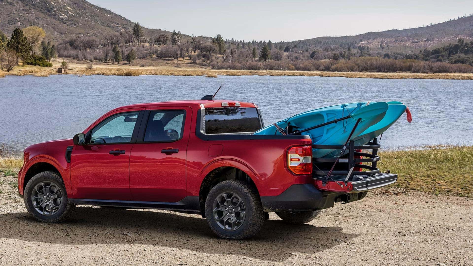 Red Ford Maverick XLT parked by a lake with kayaks secured in its cargo bed