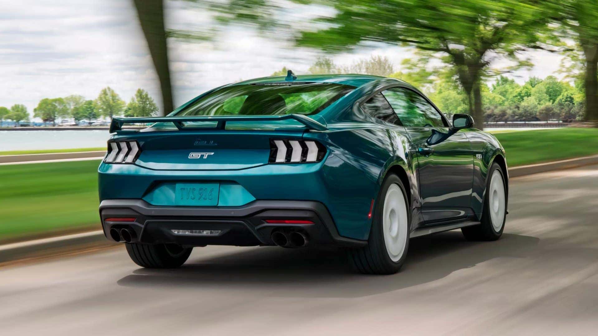 Green 2026 Ford Mustang GT driving on a tree-lined road, viewed from the rear