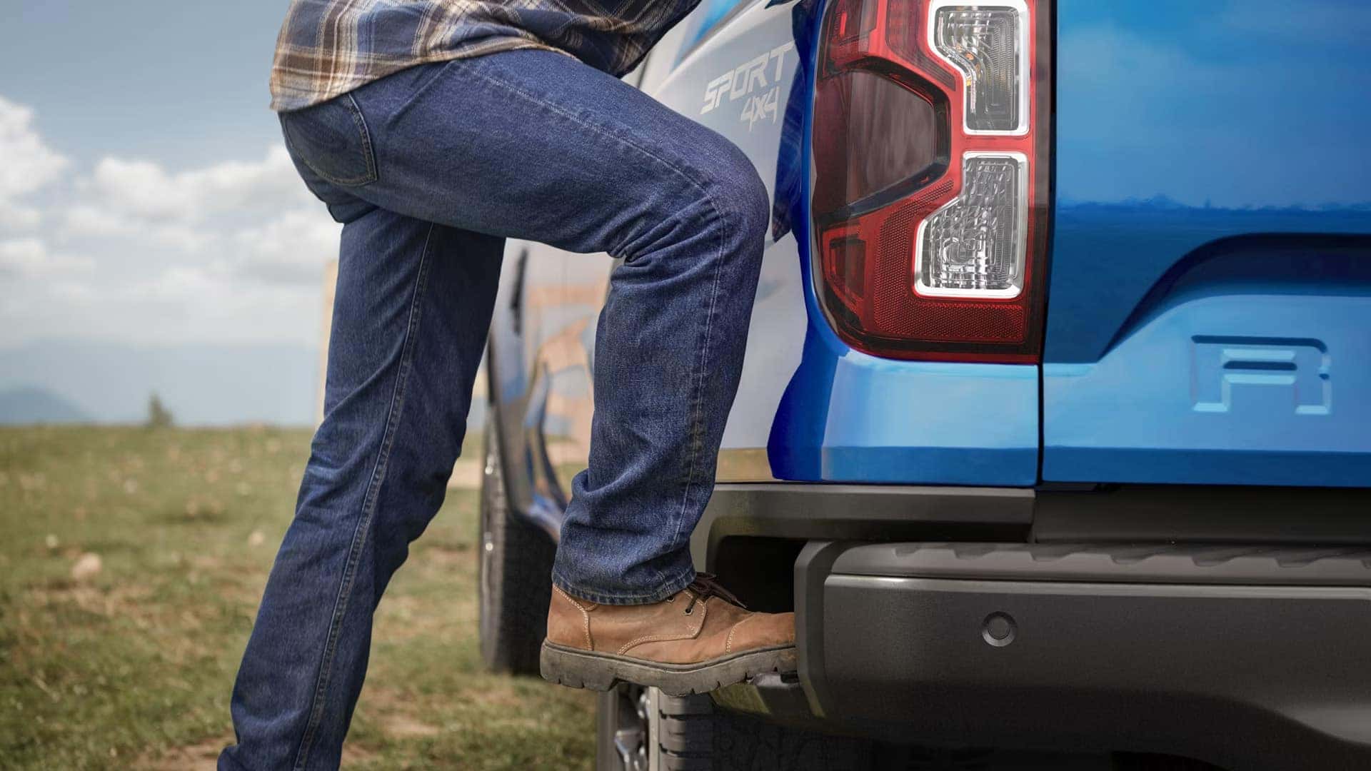 Person using the integrated rear box side step on a blue 2026 Ford Ranger Sport 4x4