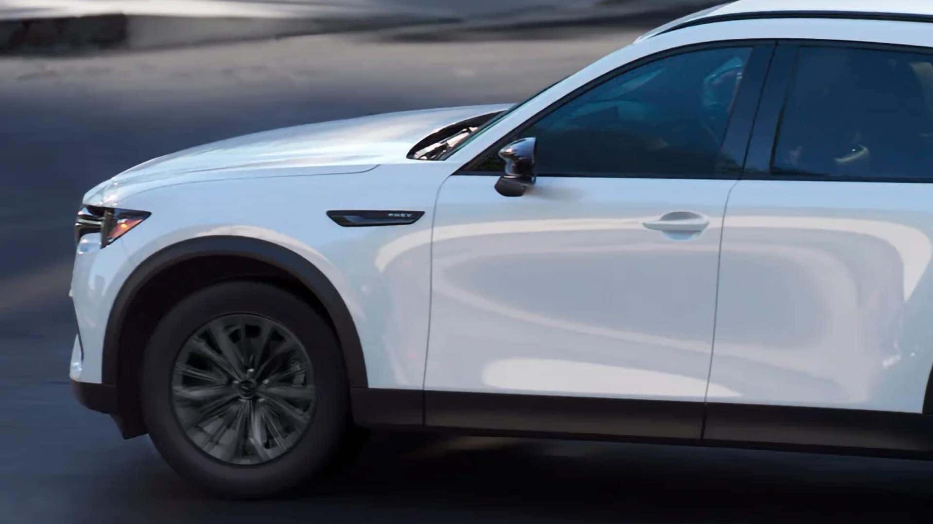 White 2026 Mazda CX-70 PHEV driving in side profile with its PHEV fender badge visible