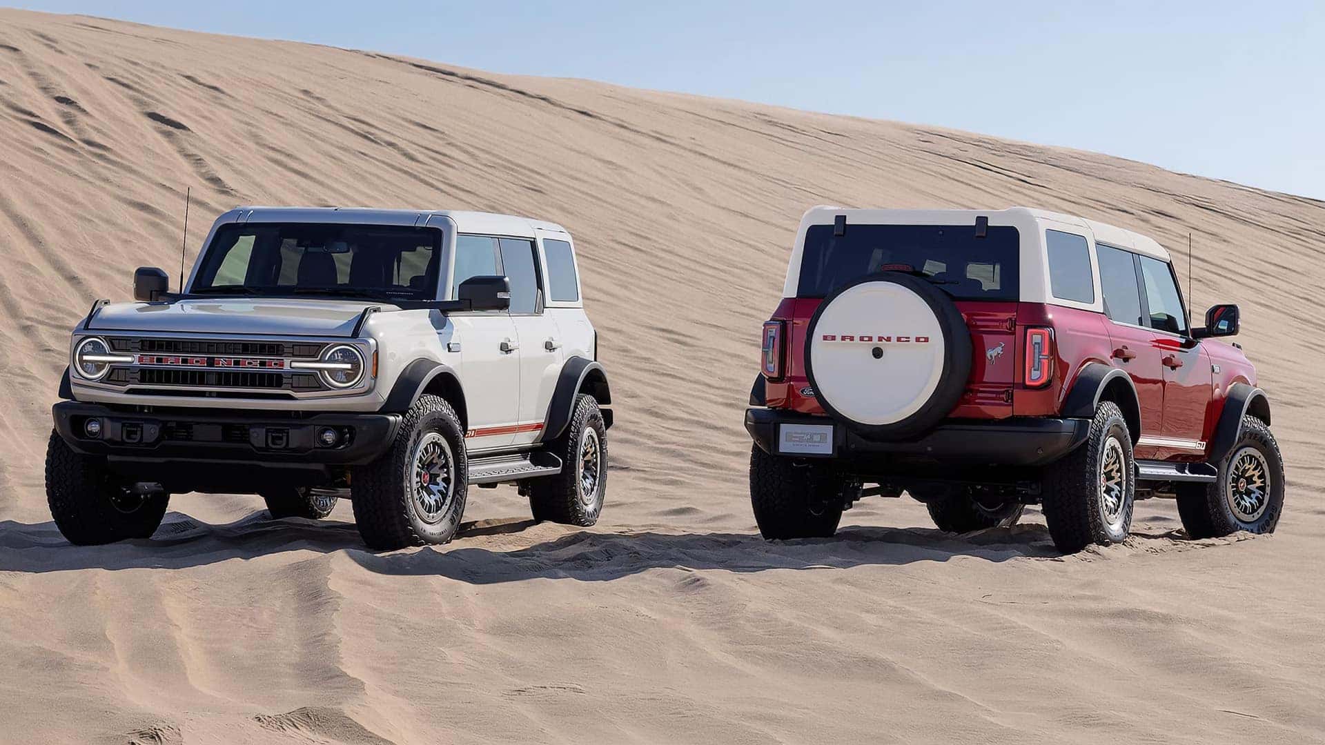 White and red 2026 Ford Bronco SUVs shown from the front and rear on sand dunes