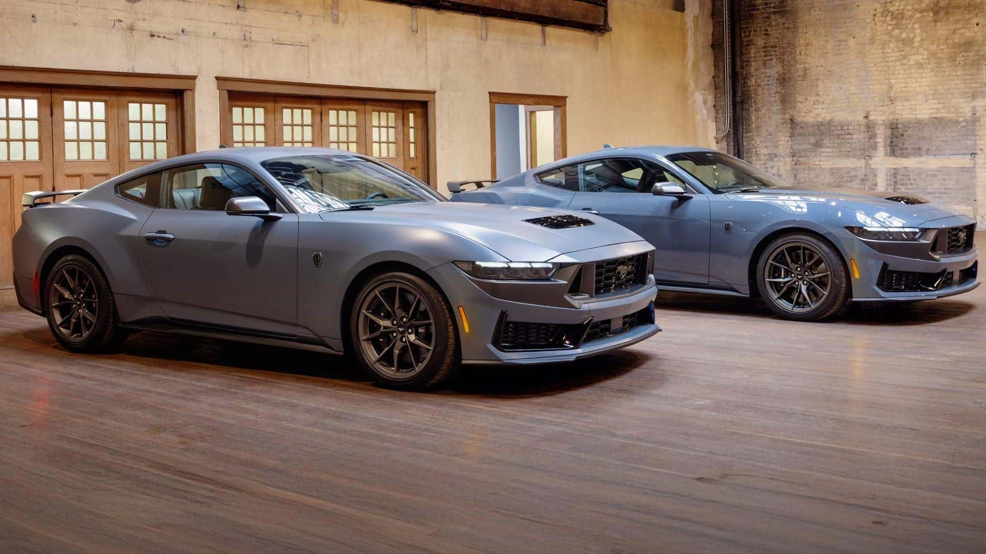 Two 2026 Ford Mustang models displayed indoors in different exterior finishes