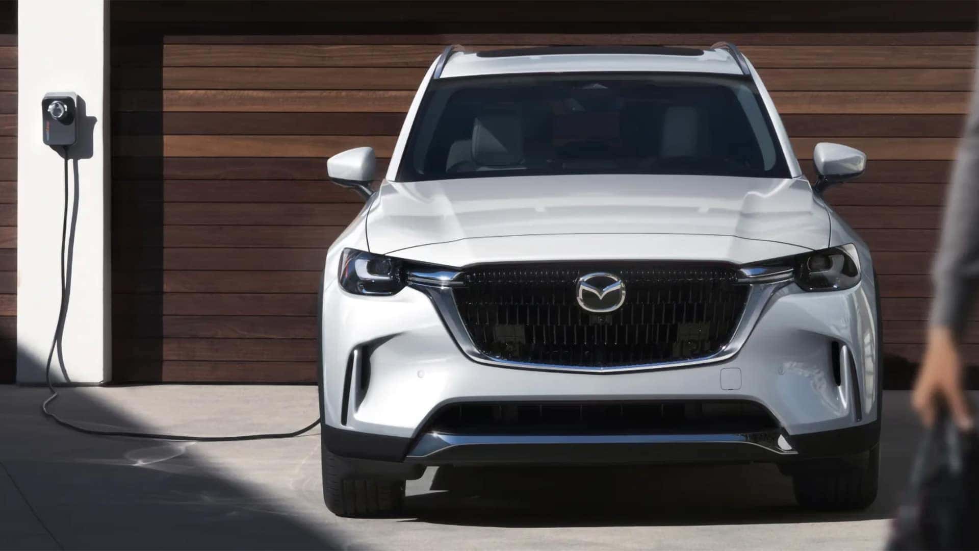 White 2026 Mazda CX-90 PHEV parked beside home electric vehicle charging equipment