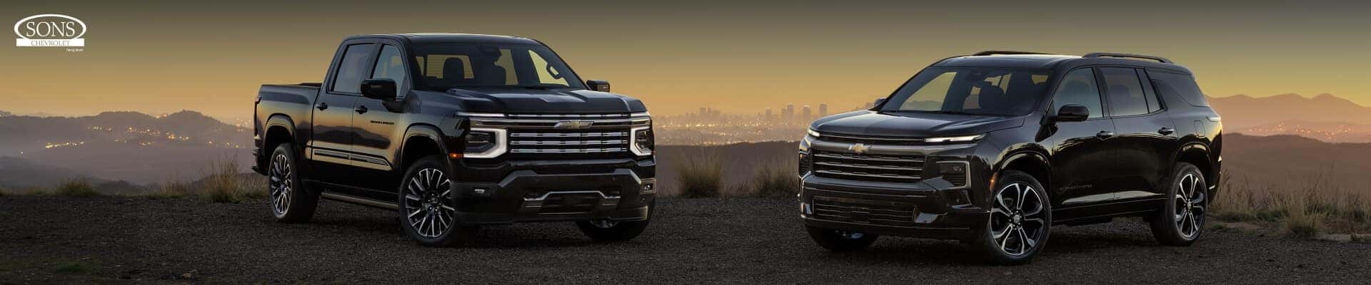 Front three-quarter view of a 2027 Chevrolet Silverado 1500 and Traverse High Country in Black parked on a scenic overlook.