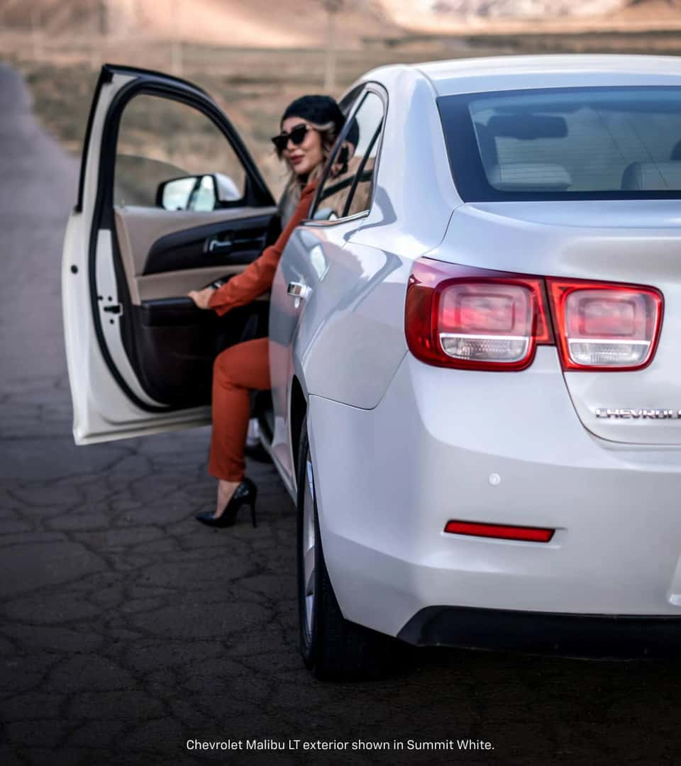 Rear view of a woman entering a 2016 Chevrolet Malibu LT in Summit White on a rural roads.