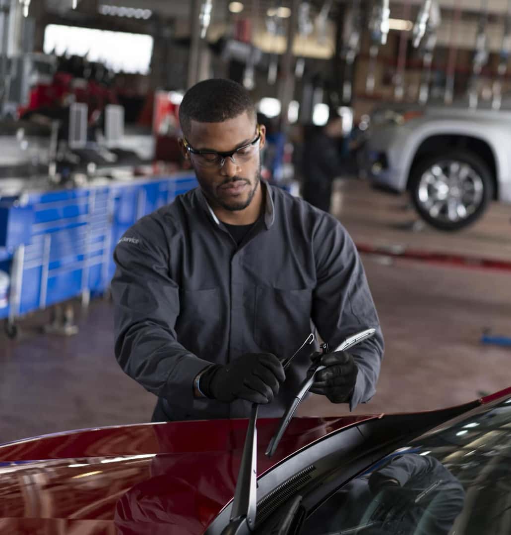 Service technician replacing windshield wiper blades on a Chevrolet vehicle in a dealership service bay.