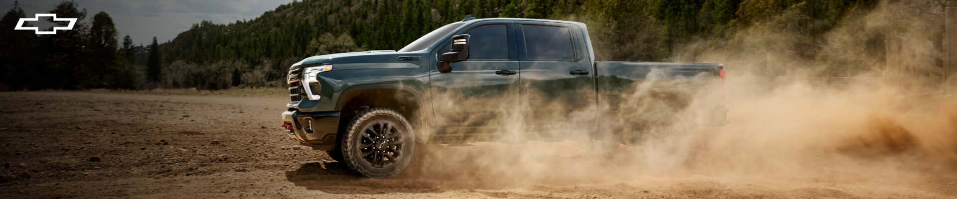 Side profile view of a 2026 Chevrolet Silverado 2500 HD ZR2 in Lakeshore Blue Metallic kicking up dust on a dirt trail.
